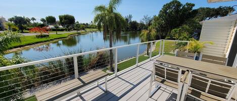 A wooden deck with a railing overlooking a calm lake and a landscaped garden.