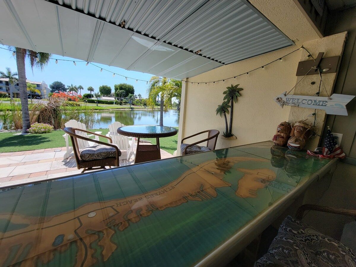 Un espace extérieur abrité, doté d’une table à plateau en verre, de chaises en osier et d’une pancarte de bienvenue.