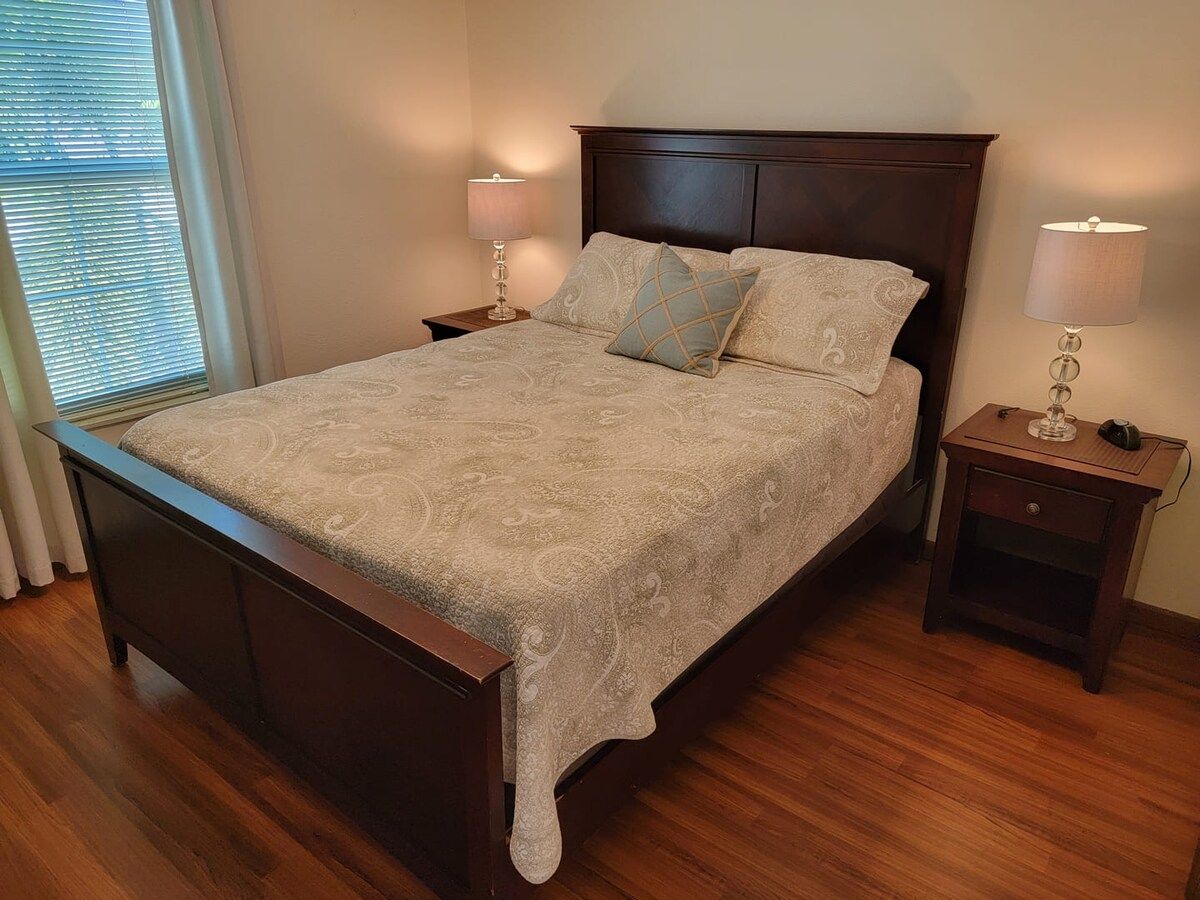 A bedroom with a wooden bed, two bedside tables, and a window with blinds.