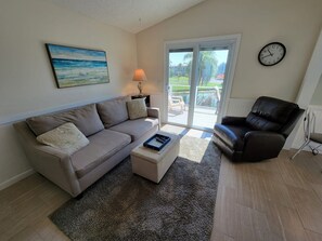 A living room with a sofa, a coffee table, a leather chair, a lamp, and a painting on the wall. - Indian Bayou Lake House 1 - Lakeside Oasis (Fort Myers Beach)