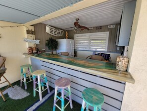 Una zona de bar con mostrador, taburetes y refrigerador.