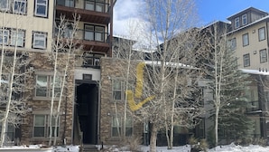 Un edificio de varios pisos con fachada de piedra, una entrada central y un estacionamiento al frente.
