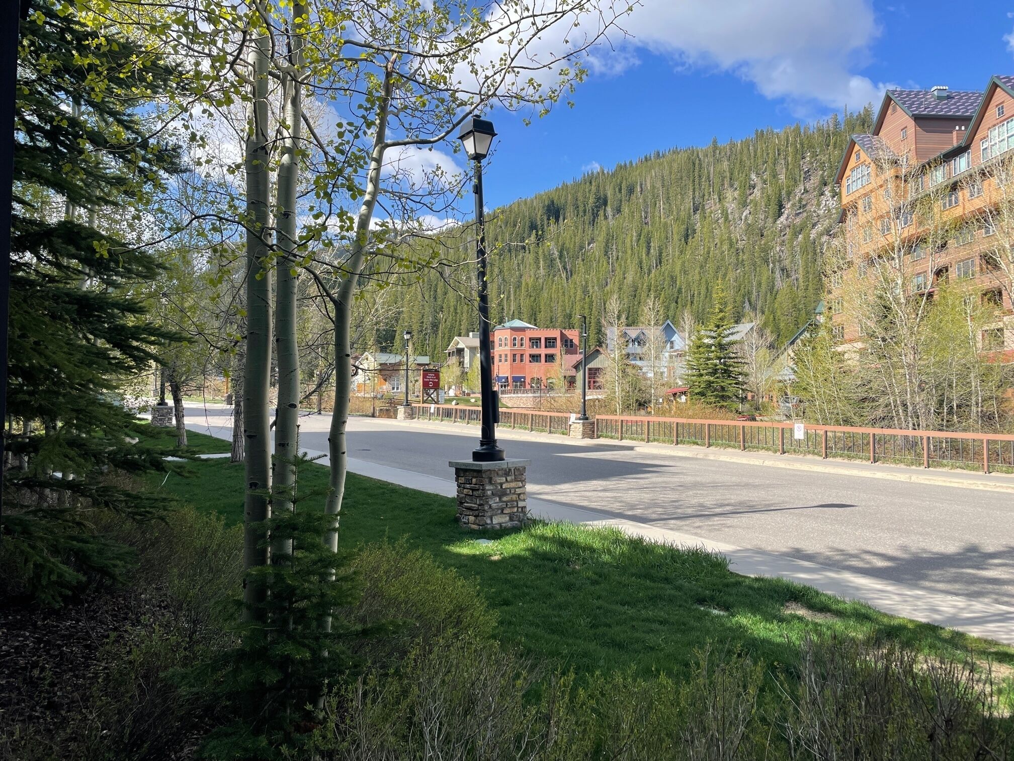 A street with a lamp post, a stone base, and a road leading to a building complex surrounded by trees and hills.