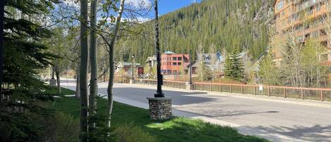 A street with a lamp post, a stone base, and a road leading to a building complex surrounded by trees and hills.