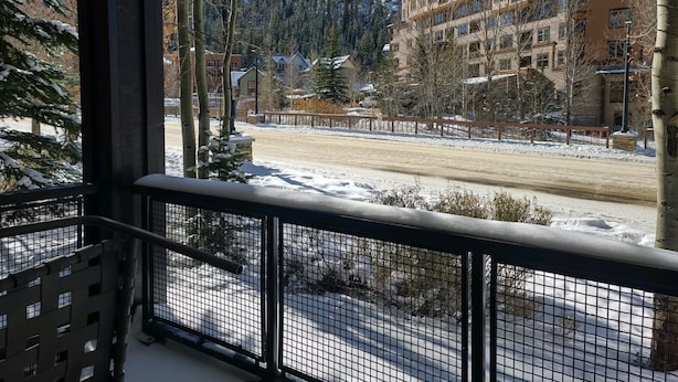 Vista desde un balcón con suelo nevado, una valla de madera y edificios al fondo.