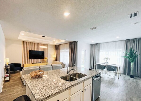 Relax in a spacious living area with a sofa and flat-screen TV, plus a kitchen with a dining table and potted plant.