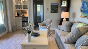 A living room with a white coffee table, a grey sofa, wicker chairs, a large clock, and a painting on the wall.