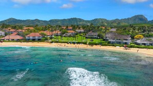 A coastal resort with beachfront villas, clear turquoise waters, and lush green hills in the background.