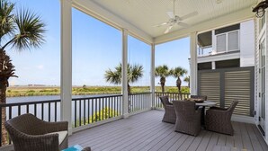 Une terrasse extérieure couverte, aménagée avec des meubles en osier, un billard et offrant une vue sur un plan d’eau et des palmiers.