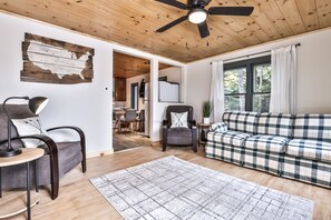 Ein gemütliches Wohnzimmer mit einem karierten Sofa, einem dunklen Sessel und einem hölzernen Deckenventilator.