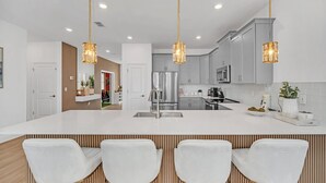 A modern kitchen with a central island, white cabinetry, stainless steel appliances, and pendant lighting.
