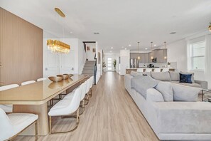 A modern open-plan living area with a dining table, sofas, and a kitchen in the background.