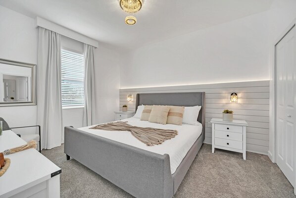 A bedroom with a large bed, bedside tables, a nightstand, a mirror, and a chandelier.