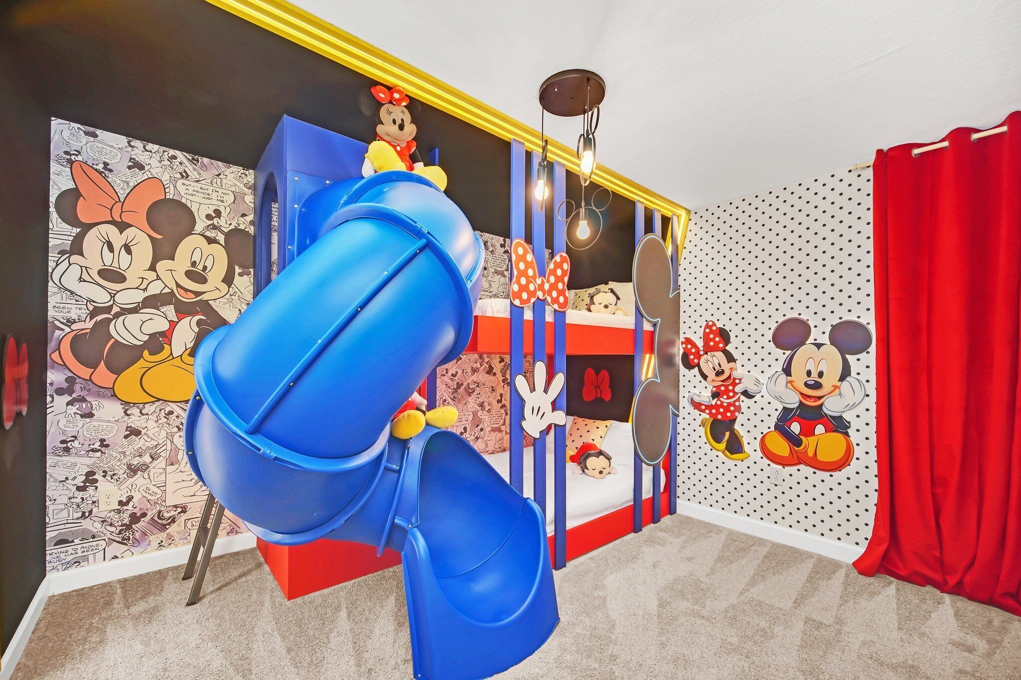 A children's play area with a blue slide, Mickey and Minnie Mouse decorations, and a bed with a polka dot pattern.