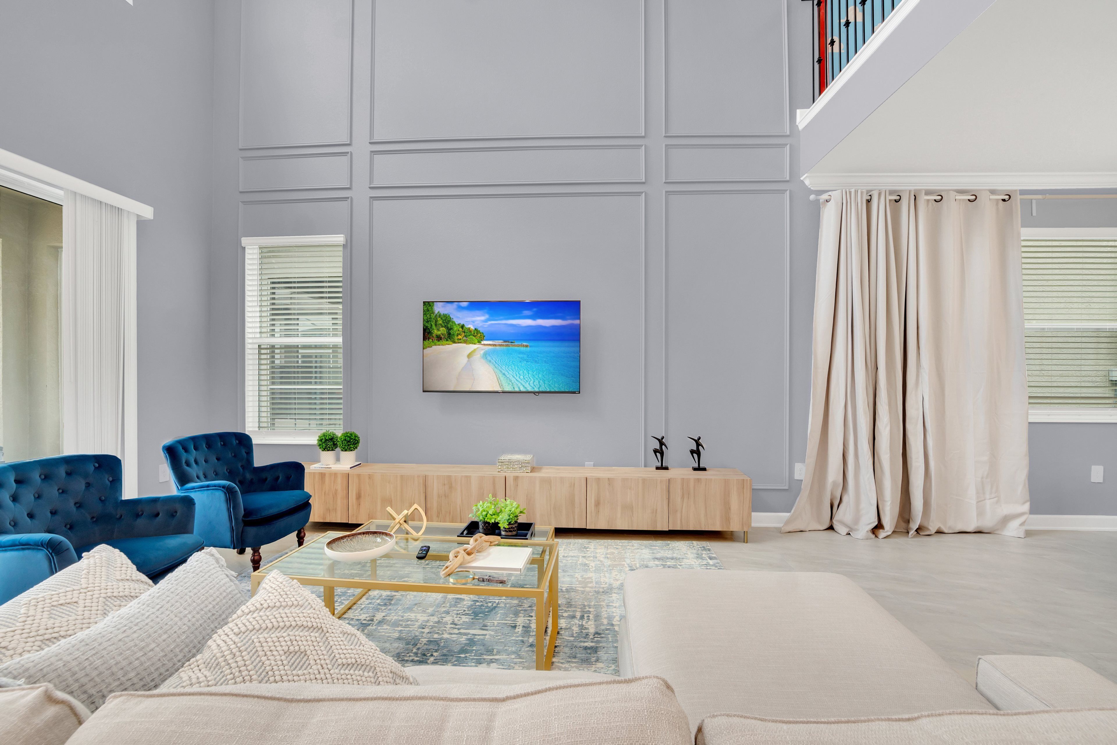 Un salon moderne avec un grand téléviseur à écran plat, des fauteuils bleus, un canapé beige et une table basse en bois.