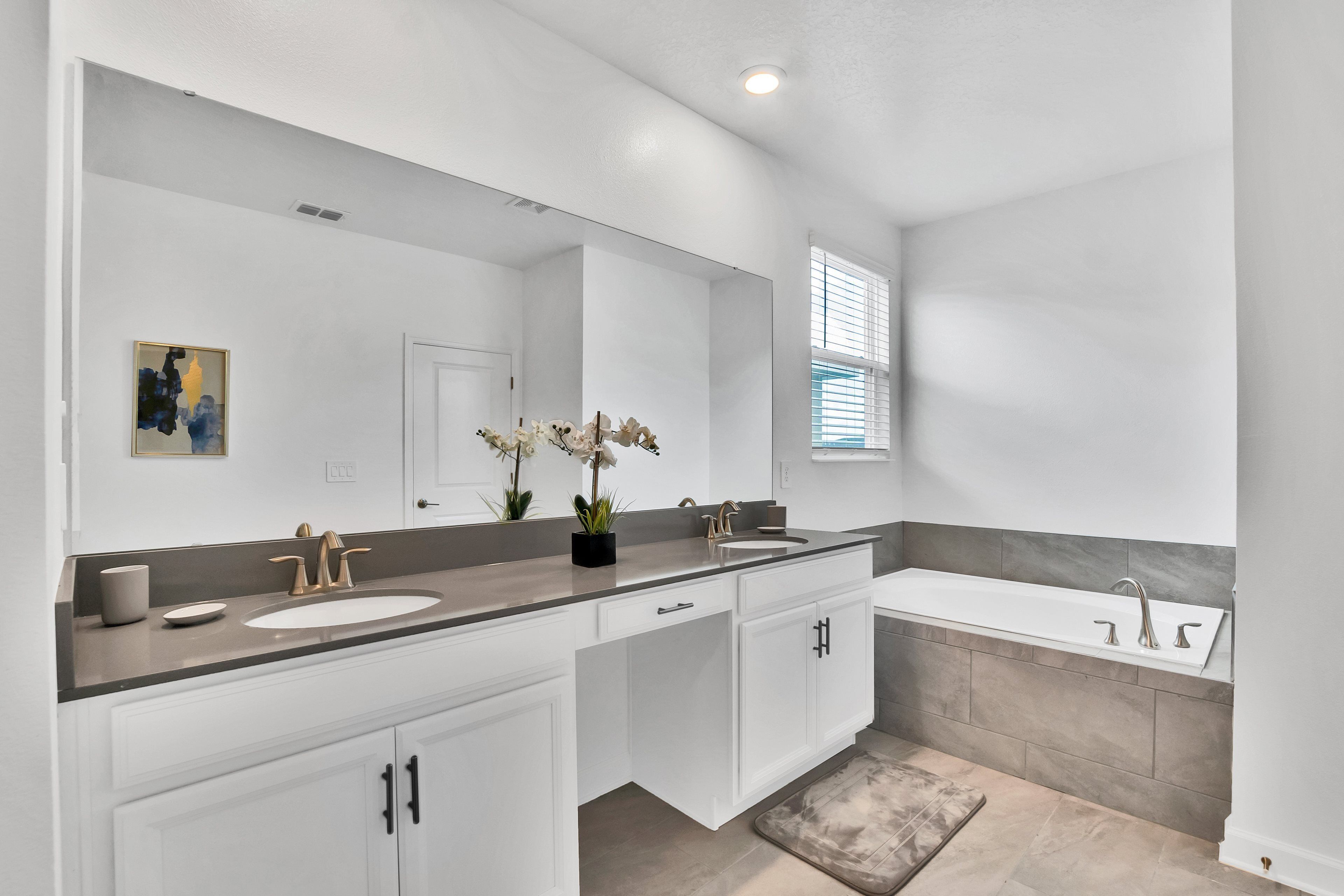 A modern bathroom with a double sink vanity, a large mirror, and a bathtub.