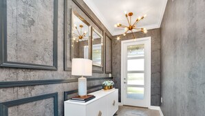 A hallway with a white console table, a large mirror, and a modern chandelier.