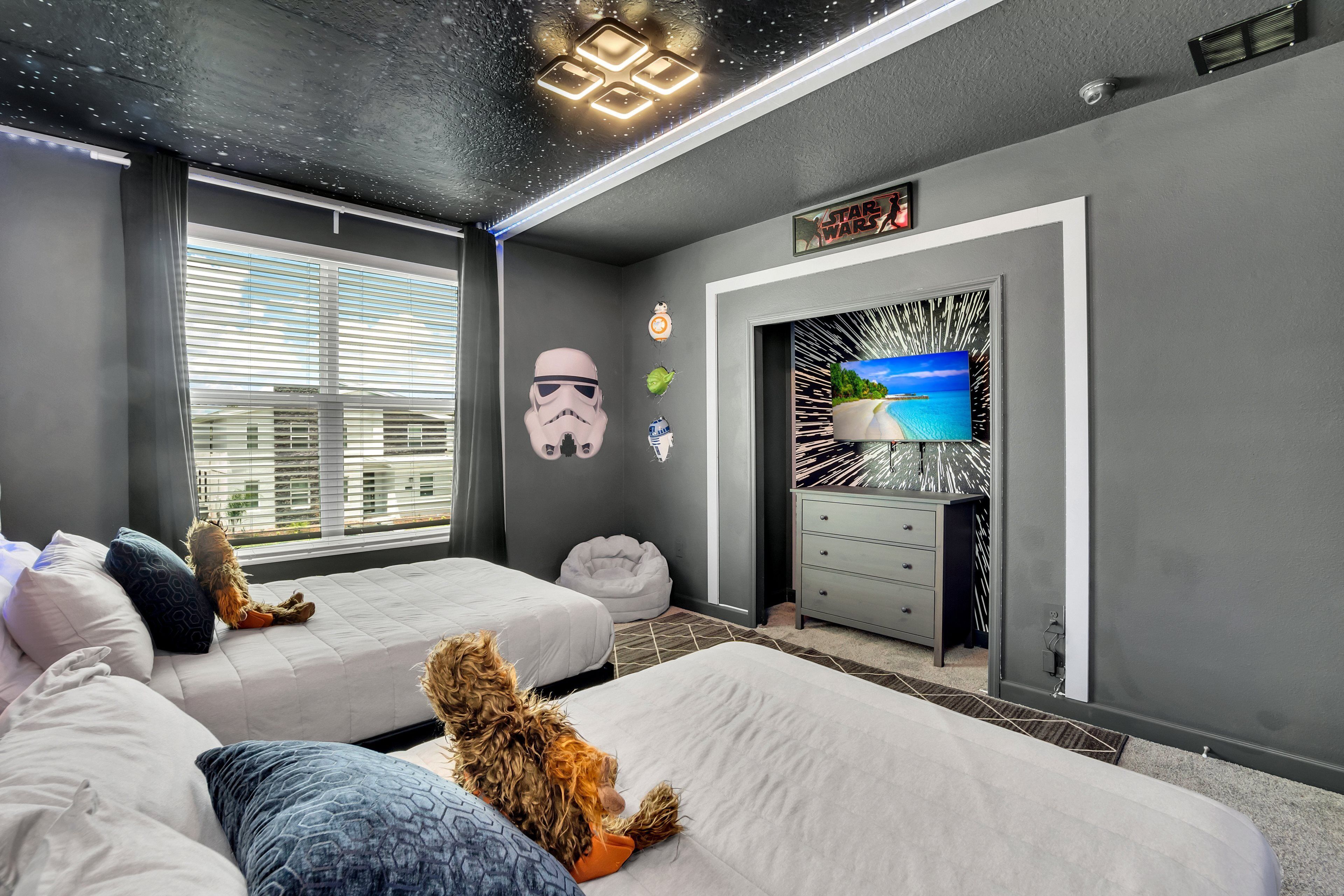 A modern bedroom with two beds, Star Wars decorations, a TV, and a city view.