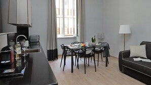A modern living room with a black sofa, a dining table with chairs, a coffee table, and a lamp. - Monti Apartments - M5 (Rome)