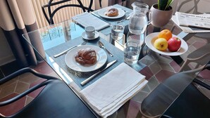 A dining table set with a croissant, a plate of fruit, a pitcher, and a newspaper.