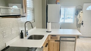 A modern kitchen with a stainless steel stove, double sink, wooden cabinets, and a large window providing natural light. - Cozy Modern Home  (Lake Placid)