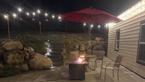 An outdoor patio with a fire pit, seating, and string lights. - Cozy Modern Home  (Lake Placid)
