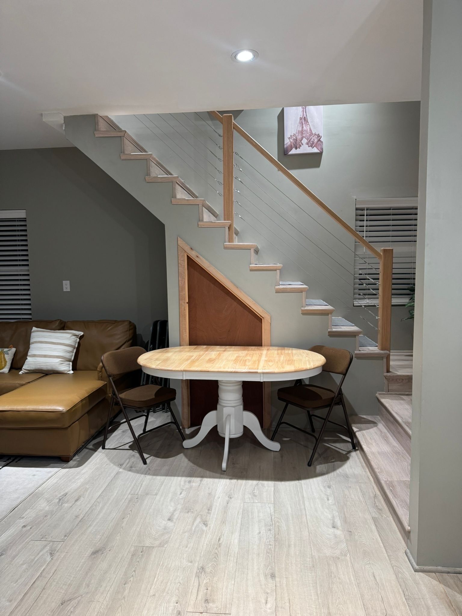 Een moderne woonkamer met een houten trap, een ronde eettafel met stoelen, en een bruine leren bank.