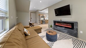 A modern living room with a sofa, ottoman, and a fireplace. - Cozy Modern Home  (Lake Placid)