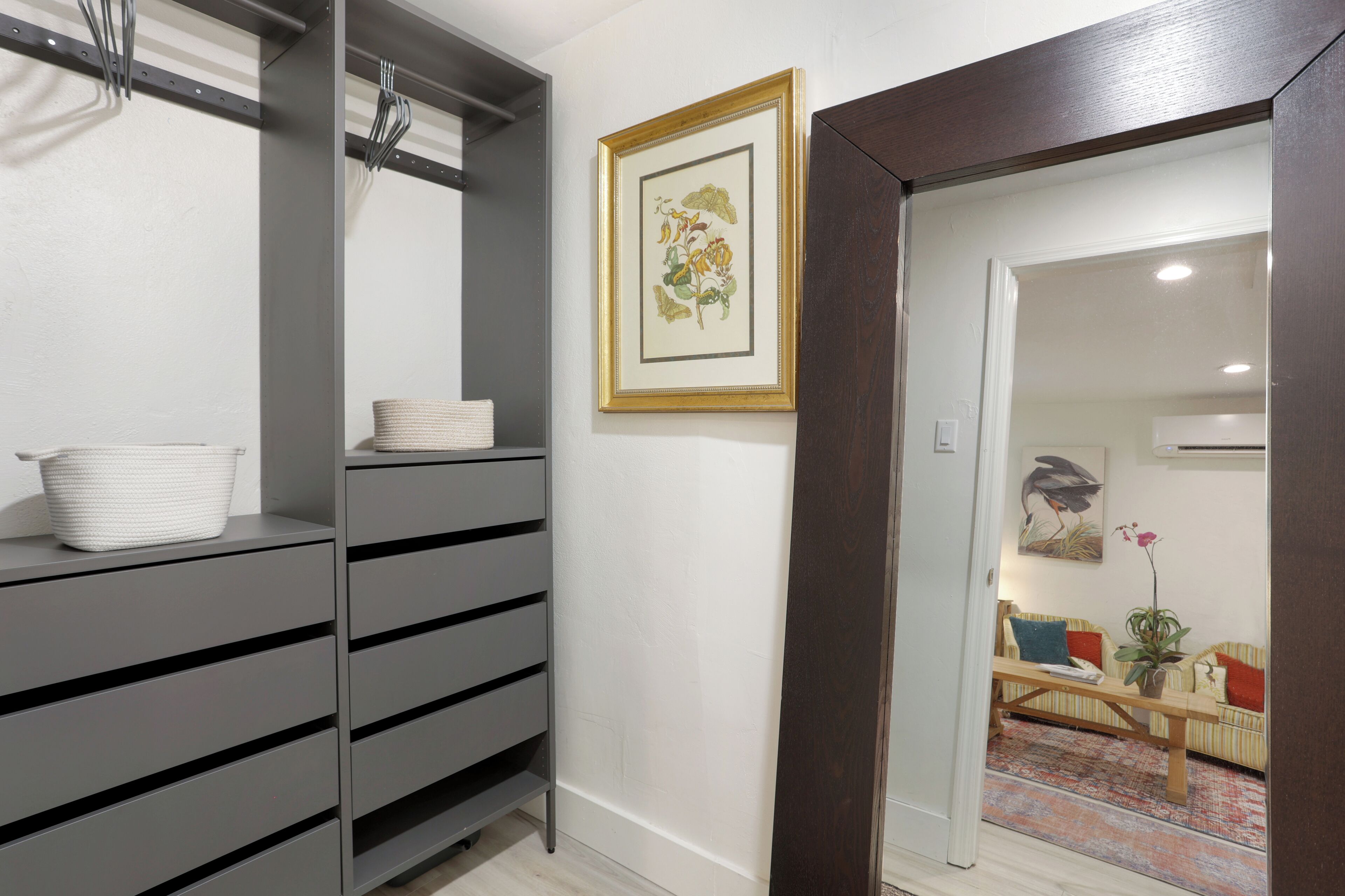 Un interior moderno con armarios grises, una impresión botánica enmarcada en la pared y un banco de madera con cojines.