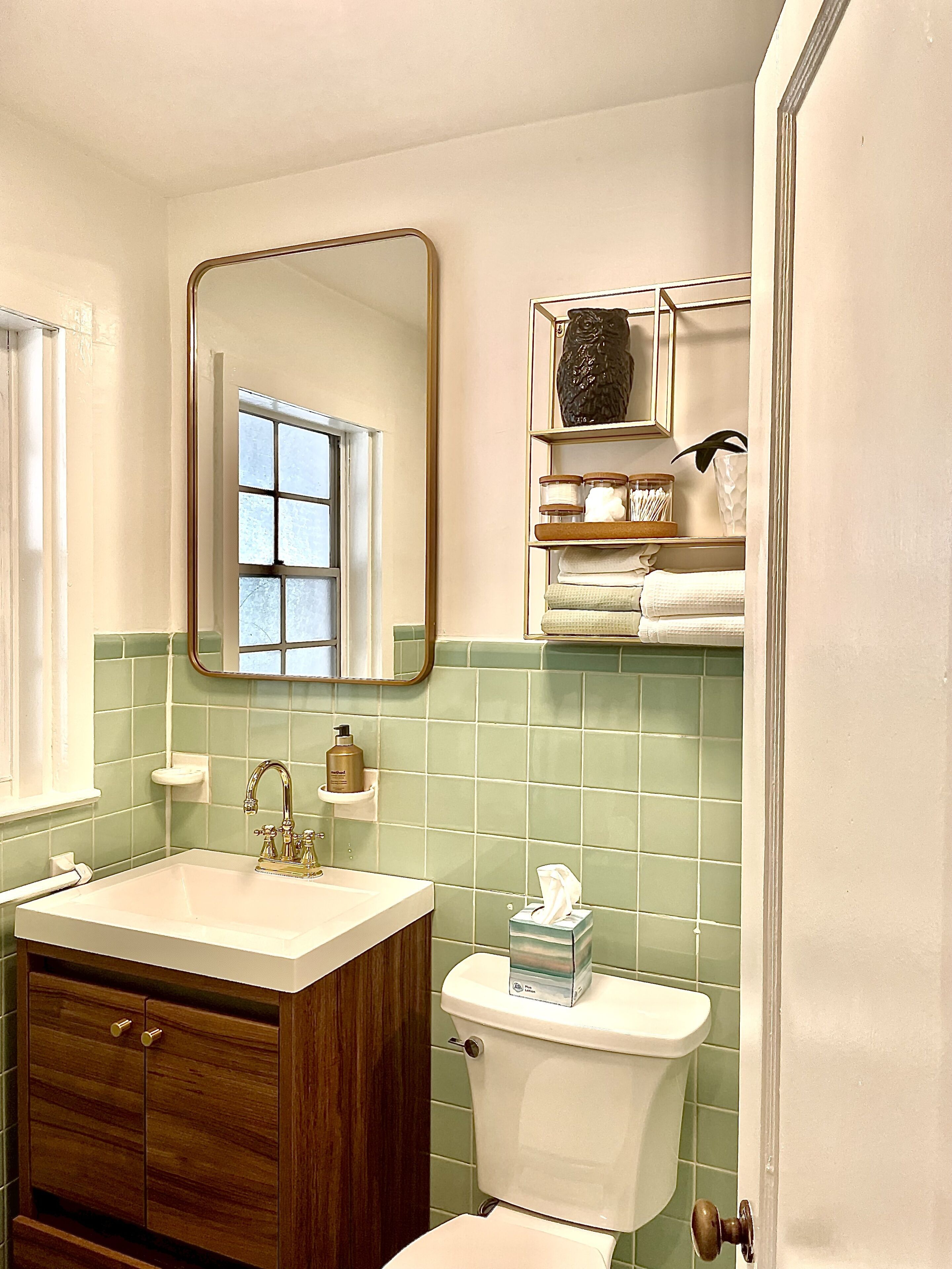 A bathroom with a sink, mirror, toilet, and green-tiled walls.