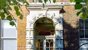 Un bâtiment traditionnel en briques, avec une porte blanche, le numéro 5, et une clôture en fer noir.