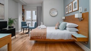 Une chambre d’hôtel moderne avec un lit en bois, un bureau, une chaise, une télévision et une plante en pot.