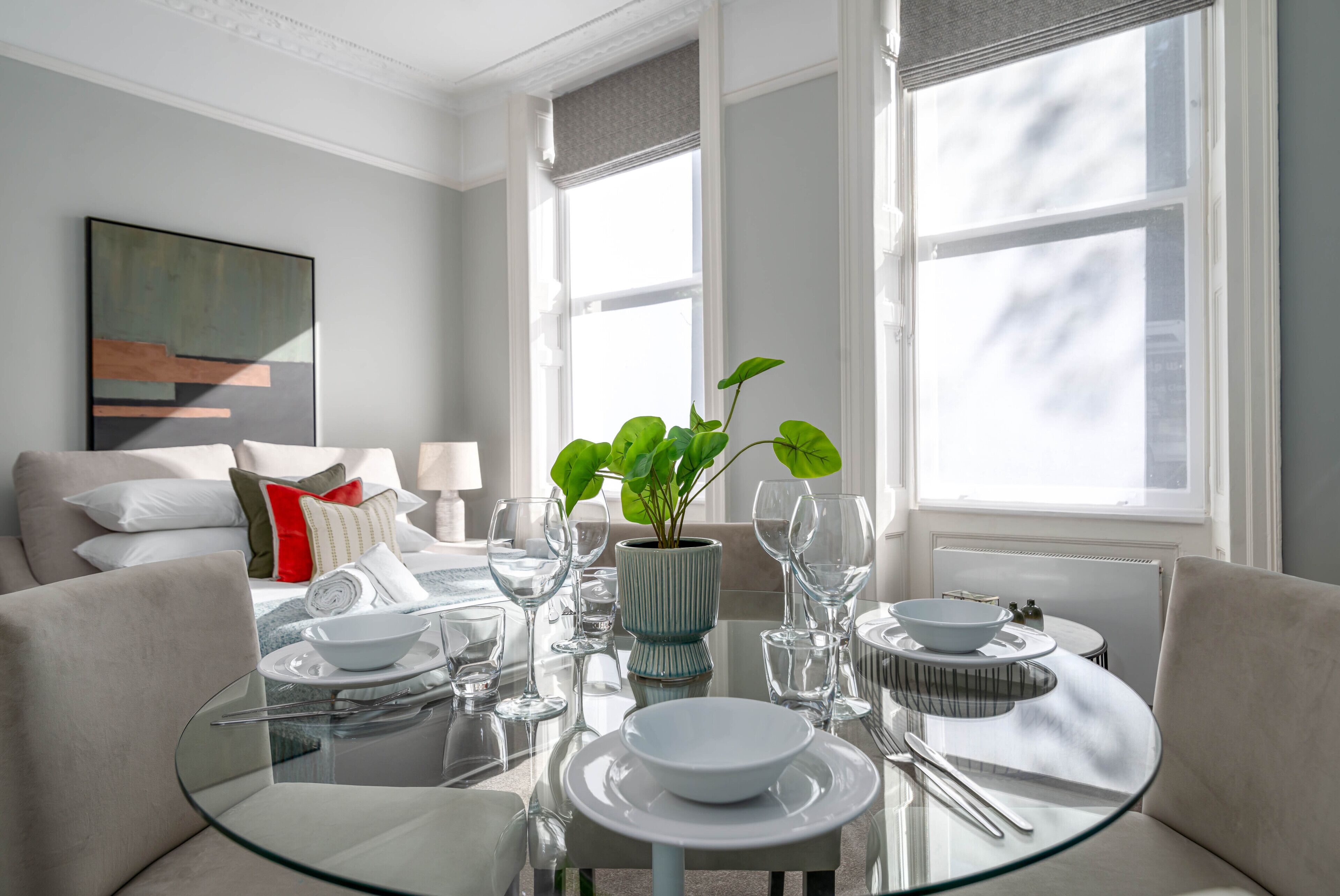 A modern dining area with a glass table, white plates, and a potted plant.