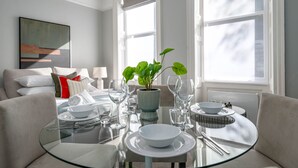 Un espace repas moderne avec une table en verre, de l’assiette blanche et une plante en pot.
