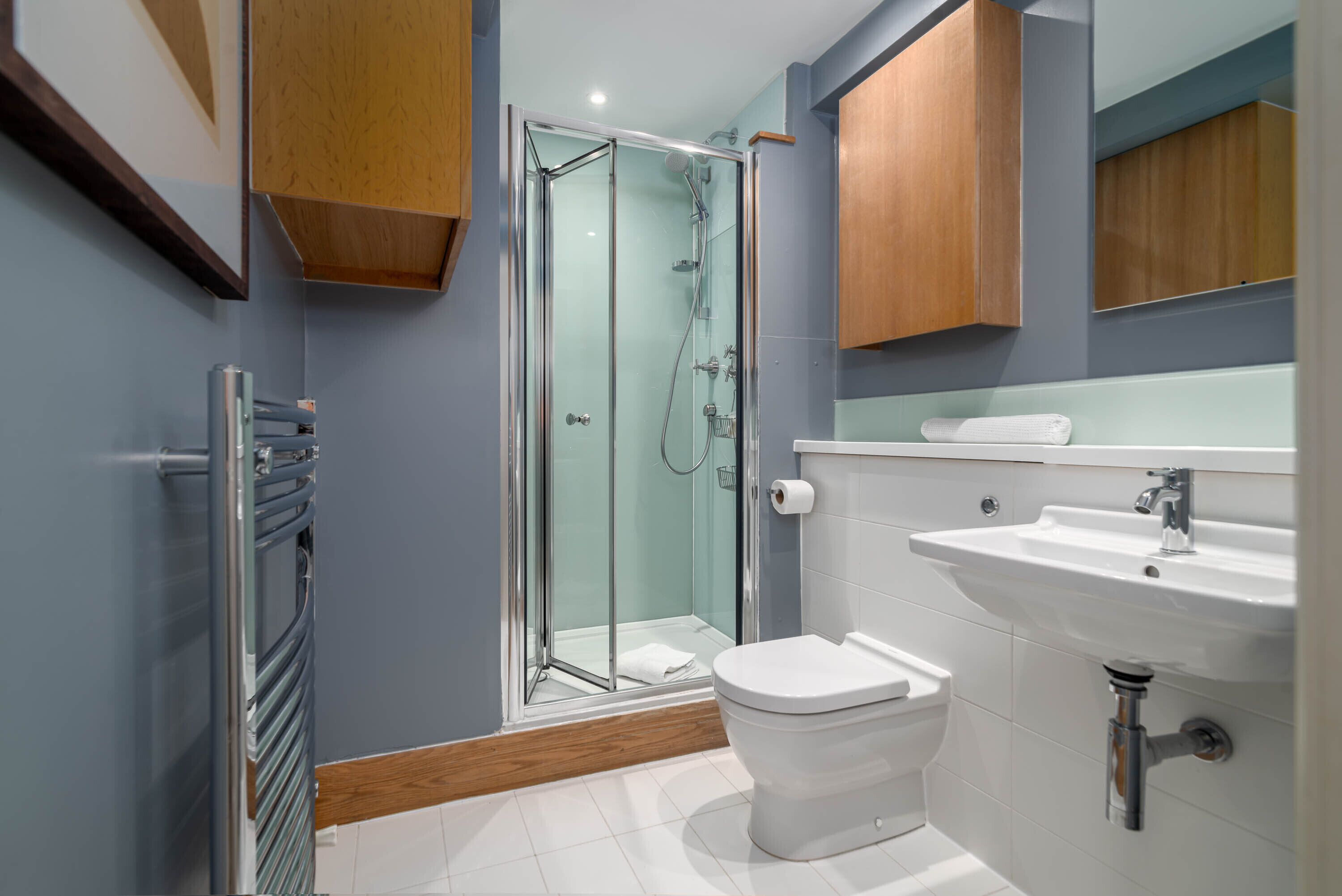 Un baño moderno con ducha de mampara de vidrio, inodoro blanco y lavamanos con espejo.