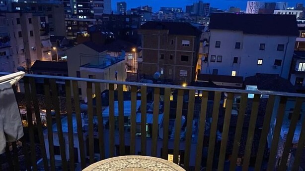 Un balcon avec une table ronde et deux chaises, un sol carrelé et une vue sur le paysage urbain au crépuscule.
