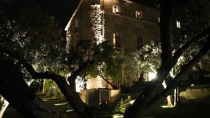 A stone building at night with illuminated windows and trees in the foreground. - Castel D'Arno THE KITCHEN Apt (Perugia)