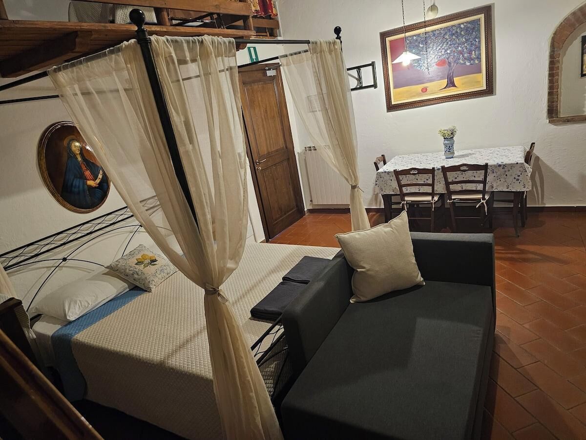 A bedroom with a bed, a sofa, a dining table, and a painting on the wall.