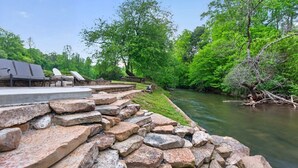 Un patio junto al río con escalones de piedra, asientos al aire libre y abundante vegetación.