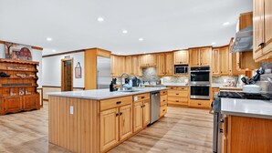 Una cocina amplia con armarios de madera, una isla central, electrodomésticos de acero inoxidable y un suelo con estampado tipo espiga.