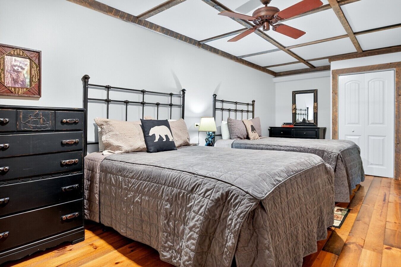 A bedroom with two beds, a dresser, a ceiling fan, and a door.