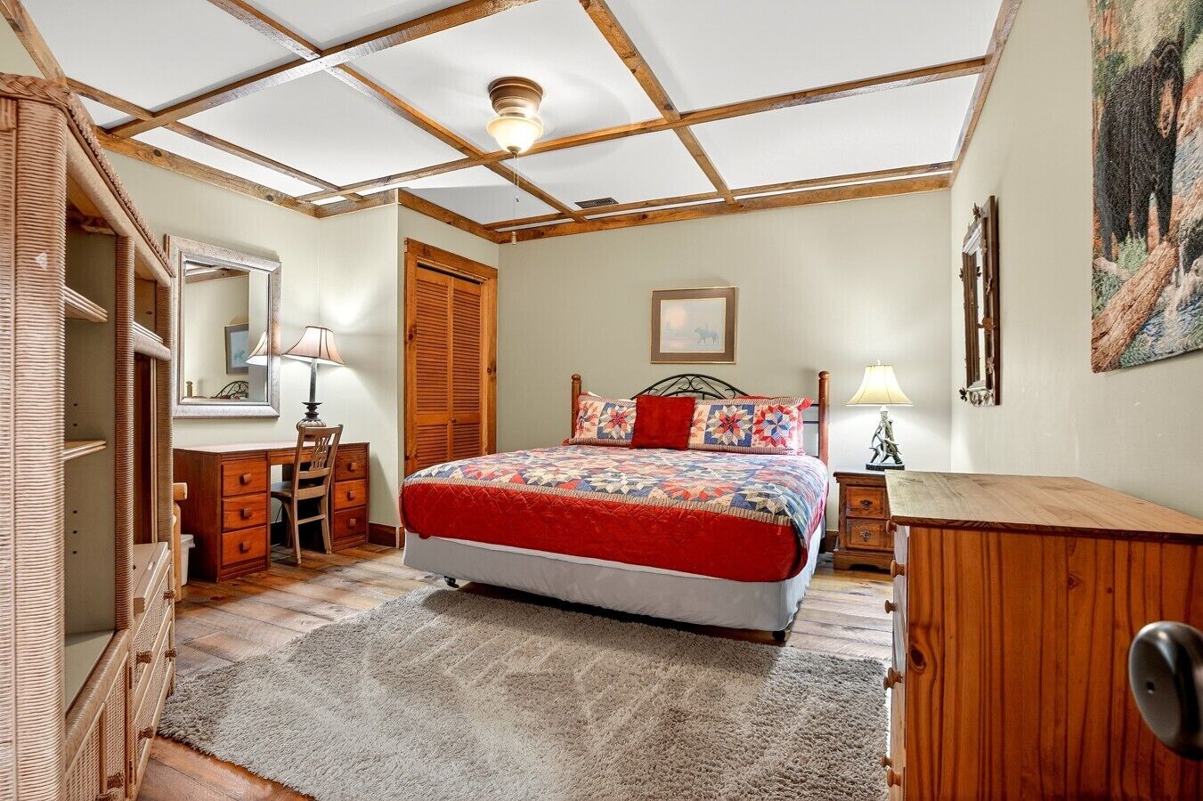 Un dormitorio con una cama, un armario de madera, un escritorio con cajones, un espejo y una puerta.