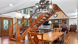 Una escalera de madera con un diseño de oso y ciervo, un comedor con una mesa y sillas de madera, y una chimenea de piedra.