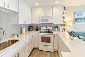 A modern kitchen with white cabinetry, a stainless steel sink, a microwave, and an oven. - Stunning Oceanfront Suite - Full Kitchen - Pool and Hot Tub! (Lincoln City)