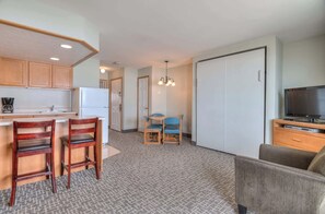 A compact hotel room with a kitchenette, a dining area, a TV, and a sliding door closet.
