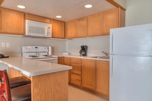Una cocina con armarios de madera, un refrigerador blanco, un microondas, una estufa y una cafetera.
