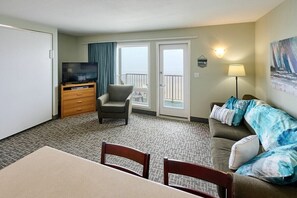 A hotel room with a television, a sofa, a chair, a dining table, and a balcony with a view.