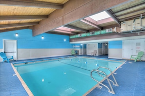 Ein heller, überdachter Swimmingpool mit klarem Wasser, blauen Fliesenwänden und einer Holzbalkendecke.