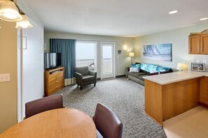 A hotel room with a dining area, a sofa, a TV, and a kitchen counter.