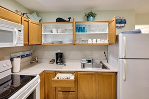 A compact kitchen with wooden cabinets, a microwave, a stove, a refrigerator, and a coffee maker.